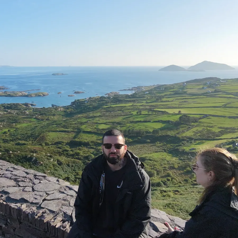 O casal sentado no muro do Farraniaragh Viewpoint, com as ilhas ao fundo